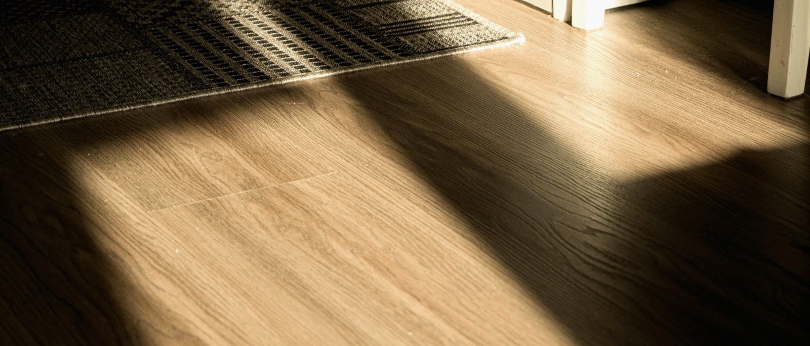 Raking daylight across a wood-effect vinyl plank floor, beside the edge of a barrier mat